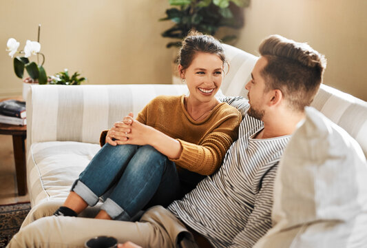 Sofa, couple and conversation with smile for joke, funny memory and bonding together in marriage. Happy people, woman and man with love embrace for admiration, commitment and connection at home - Powered by Adobe