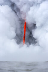 Lava tube flowing into ocean in Hawaii at dawn shows the poisonous steam rising as the hot liquid...