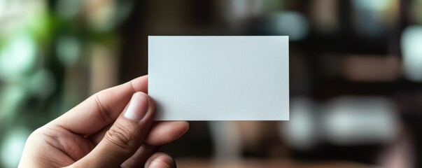 A hand holding a blank white card against a blurred background, ideal for showcasing designs or branding concepts.