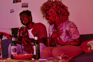 Young people sitting on sofa and singing loudly together while they illuminated with neon pink light