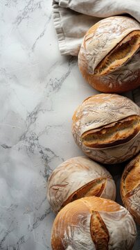 Freshly baked round loaves of bread laid out on border of vertical breadle white marble table and linen natural fabric on side top view. Space for text