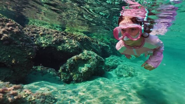 Girl child swims and snorkels under water. Kid dives into the ocean wearing goggles and looks at the underwater world. High quality 4k footage