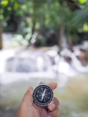 Naklejka premium Close up of compass in woman hand with waterfall as background. The concept of world tourism day, Searching the right directions and Travel