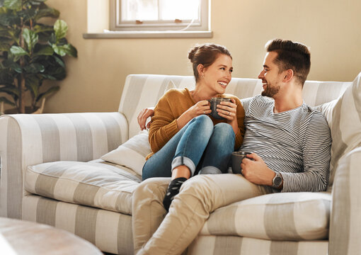 Relax, coffee or happy couple laughing on couch with smile or love in house for care, latte and bonding. Apartment, break and people drinking tea beverage on sofa together to chill in lounge in Spain