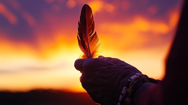 Close-up of a Native American Elder's Hand Holding an Eagle Feather Against a Dramatic Sunset with Warm Orange and Purple Hues, Symbolizing Spiritual Connection