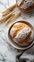 Top view of freshly baked bread sprinkled with flour served on a white plate with golden wheat ears on a marble table. Rustic and organic style perfect for bakery or cooking concept mockup.
