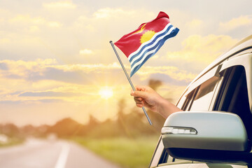 Waving the Kiribati flag against the sunrise or sunset from a car driving along a country road. Holding the Kiribati flag, traveling by car, on a weekend trip.