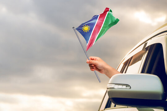 Waving the Namibia flag against the sunrise or sunset from a car driving along a country road. Holding the Namibia flag, traveling by car, on a weekend trip.