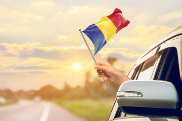 Waving the Romania flag against the sunrise or sunset from a car driving along a country road. Holding the Romania flag, traveling by car, on a weekend trip.