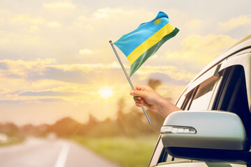 Waving the Rwanda flag against the sunrise or sunset from a car driving along a country road. Holding the Rwanda flag, traveling by car, on a weekend trip.