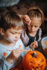 Fototapeta premium Two children painting a pumpkin with orange paint. One of the children has a white shirt on. The pumpkin is orange and has a scary face painted on it