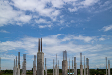 Concrete pillars of an unfinished building project rise against a bright blue sky with puffy white...