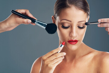 Makeup artist, model and hands with woman in studio for glamour, cosmetics and cosmetology. Foundation, brush and product with female person on gray background for glow, shine or beauty treatment