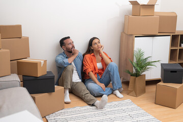 Married couple sits among boxes thinking about moving with further living in new apartment in countryside collecting various home decorations in packing boxes