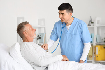 Male nurse hearing senior man with stethoscope in bedroom