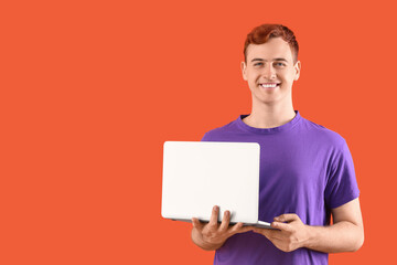 Happy young redhead man with laptop on orange background