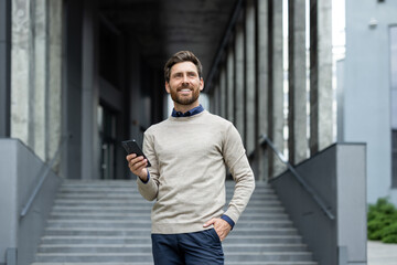 Confident businessman wearing smart casual outfit stands on modern building stairs holding...