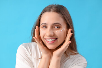 Fototapeta premium Young woman with eye cream on blue background, closeup