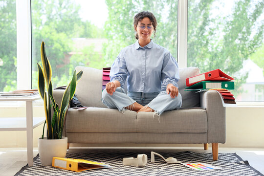 Female African-American graphic designer meditating on sofa in office