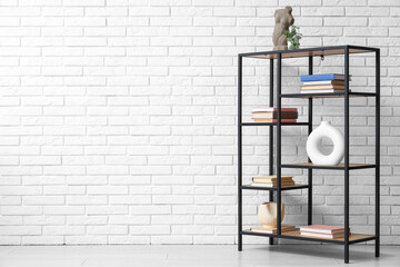 Shelving unit with stacks of books and decor near white brick wall