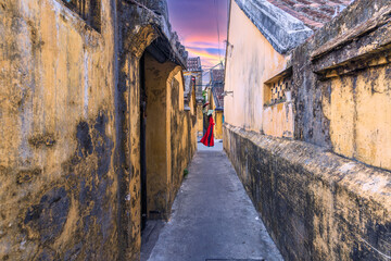 Asian woman in an ao dai costume walks in an alley in Hoi An, ancient town.
