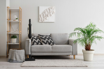 Modern vacuum cleaner on carpet near grey sofa in living room