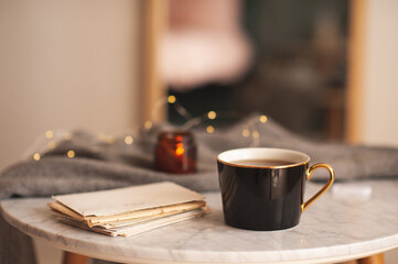 Paper handwritten letters with cup of tea and scent candle on marble coffee table in living room close up. Cozy atmosphere.
