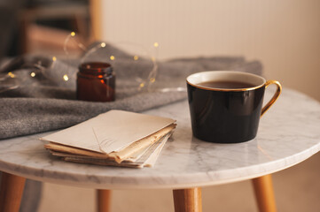 Paper handwritten letters with cup of tea and scent candle on marble coffee table in living room close up. Cozy atmosphere.