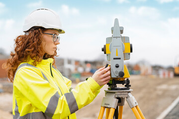 A Focused Surveyor Measures Land Meticulously on a Construction Site Under a Clear Blue Sky