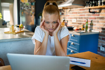 Young woman stressed while working on laptop in kitchen