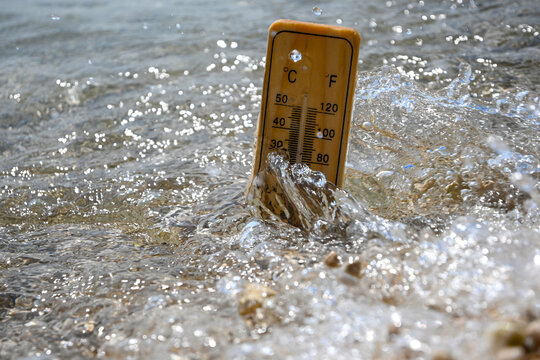 Wooden thermometer measuring increasing temperature of sea water during heat wave