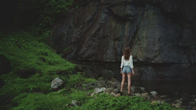 Joyful woman stands in a tropical jungle, gazing at a hidden waterfall, surrounded by lush greenery. This picturesque scene inspires wanderlust
