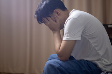 A depressed man sits at home with his hands covering his face.