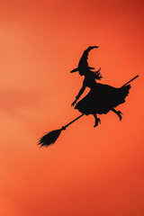 Silhouette of a witch on a broomstick on an orange background