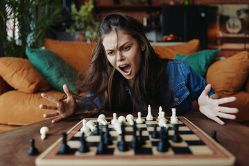 Woman playing chess with angry expression on face at table in front of couch