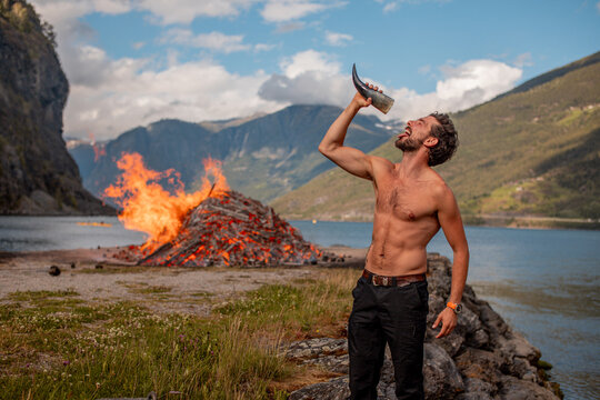 Fit young man drinking from a horn in front of a bonfire in midsommer in Norway