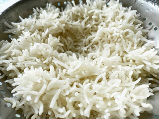 Steamed boiled rice rests on a steel strainer, with each fluffy grain separated and lightly steaming. 