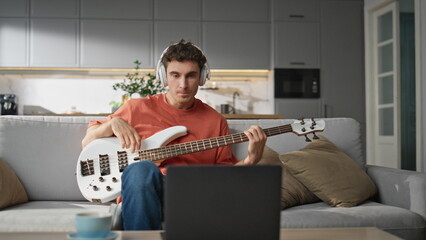 Talented man playing guitar at sofa. Handsome guy in headphones reading chords