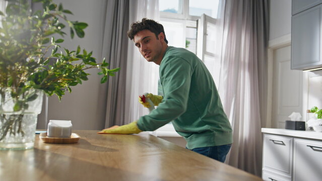Cleaning worker removing dust kitchen closeup. Positive man spraying detergent