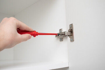 A worker installs a furniture hinge on the door of a wardrobe