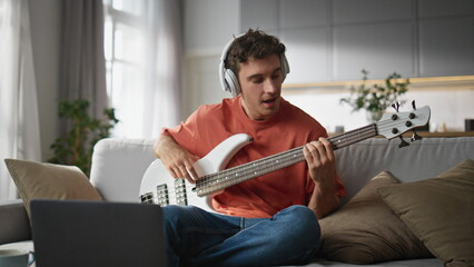 Happy musician playing guitar living room. Smiling man recording music tutorial