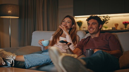 Married couple resting couch together. Smiling husband switching tv channels