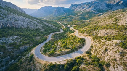 Fototapeta premium A picturesque aerial view of a road winding through a mountain range, capturing the beauty of travel by car through scenic landscapes