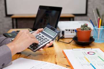 A professional hand calculating numbers with a calculator, pen in hand, while a laptop rest nearby, highlighting focus and precision in financial work.