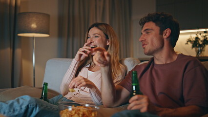 Laughing pair enjoying comedy at home weekend. Carefree spouses eating snacks