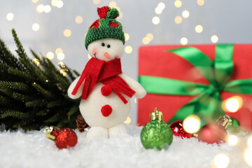 Funny snowman figure and other Christmas decor on artificial snow against blurred lights