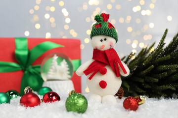 Funny snowman figure and other Christmas decor on artificial snow against blurred lights