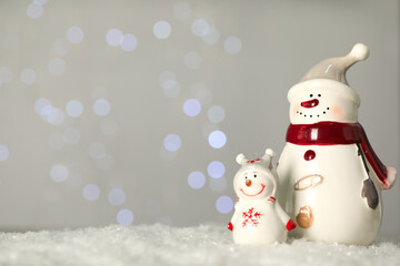 Cute decorative snowmen on artificial snow against blurred lights. Space for text