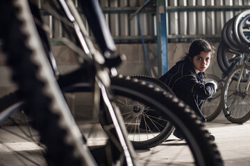 Focused young woman working on bike repair in garage, industrial setting, mechanic concept with tools and bicycles.