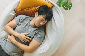 Asian man sleep over the phone on the bean bag sofa, taking a nap in the afternoon.